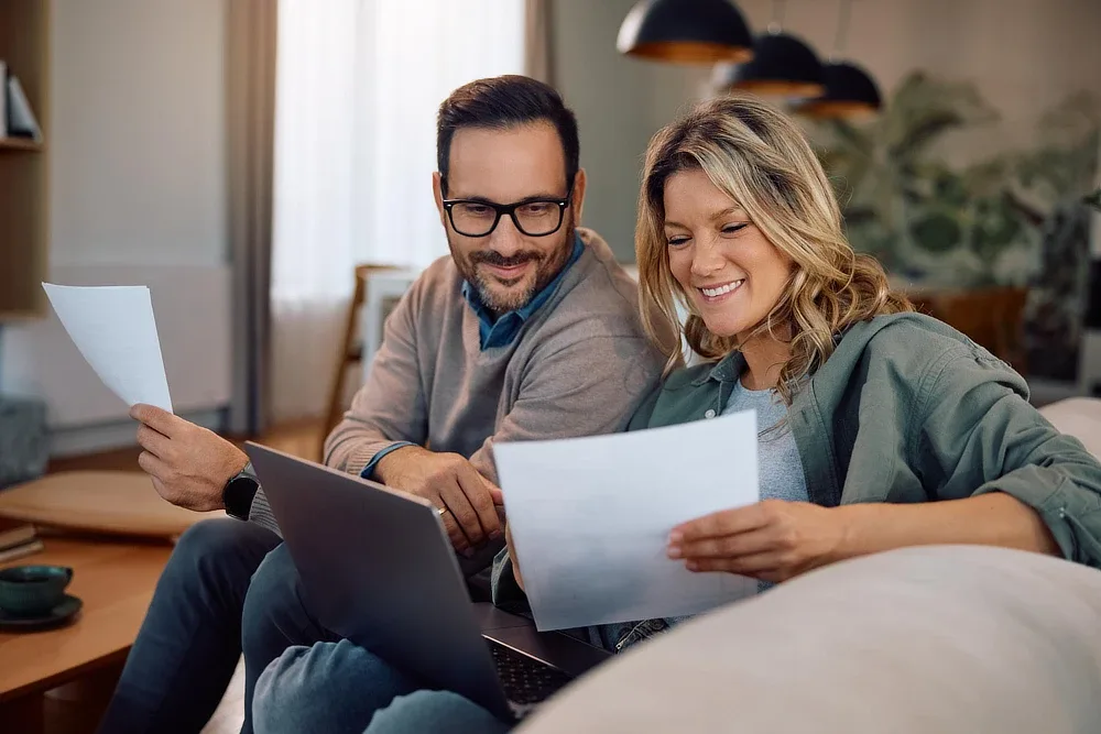A couple sitting at home reading paperwork with a laptop open