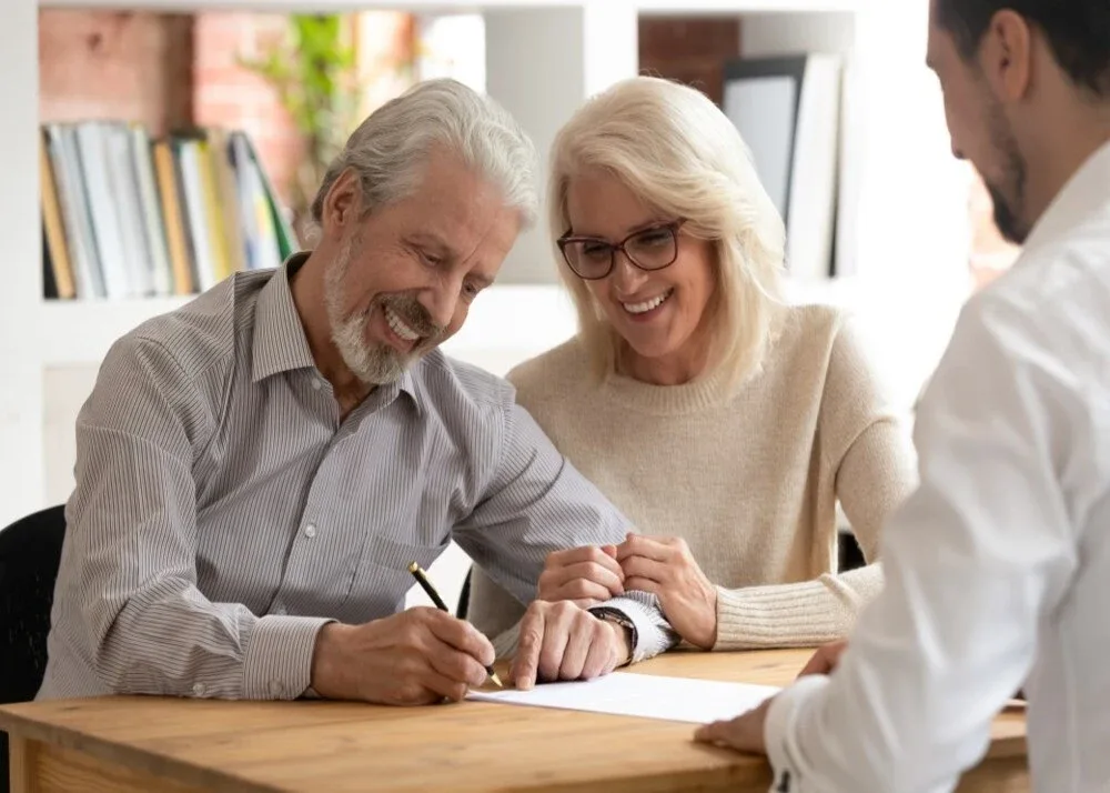 An older couple signing papers at a table with an adviser