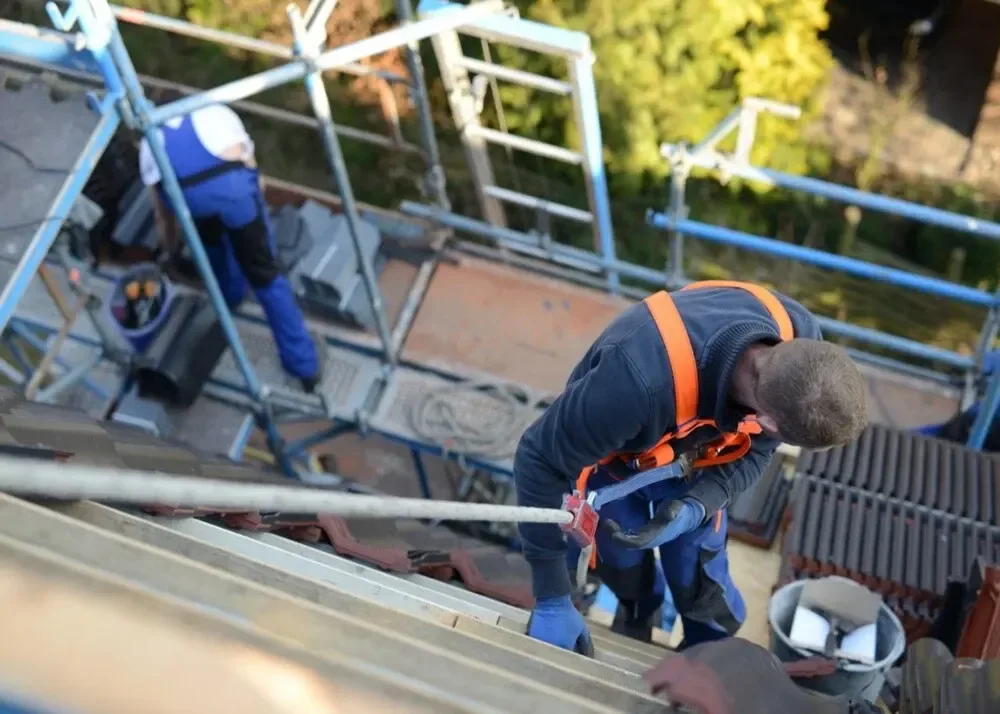Pracownicy wyposażeni w uprzęże bezpieczeństwa na podwyższonej platformie, zajmujący się montażem metalowych paneli na wysokości
